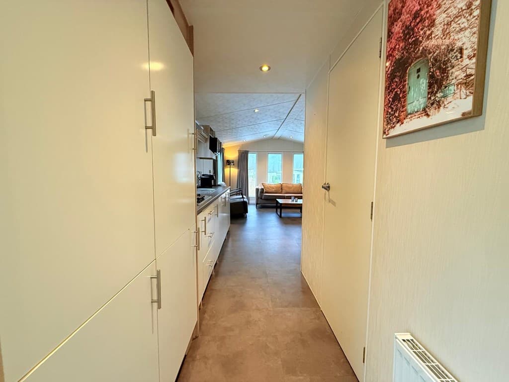 Ingang van een vakantiewoning met een lange gang, moderne keuken aan de linkerzijde en een zithoek aan het einde.