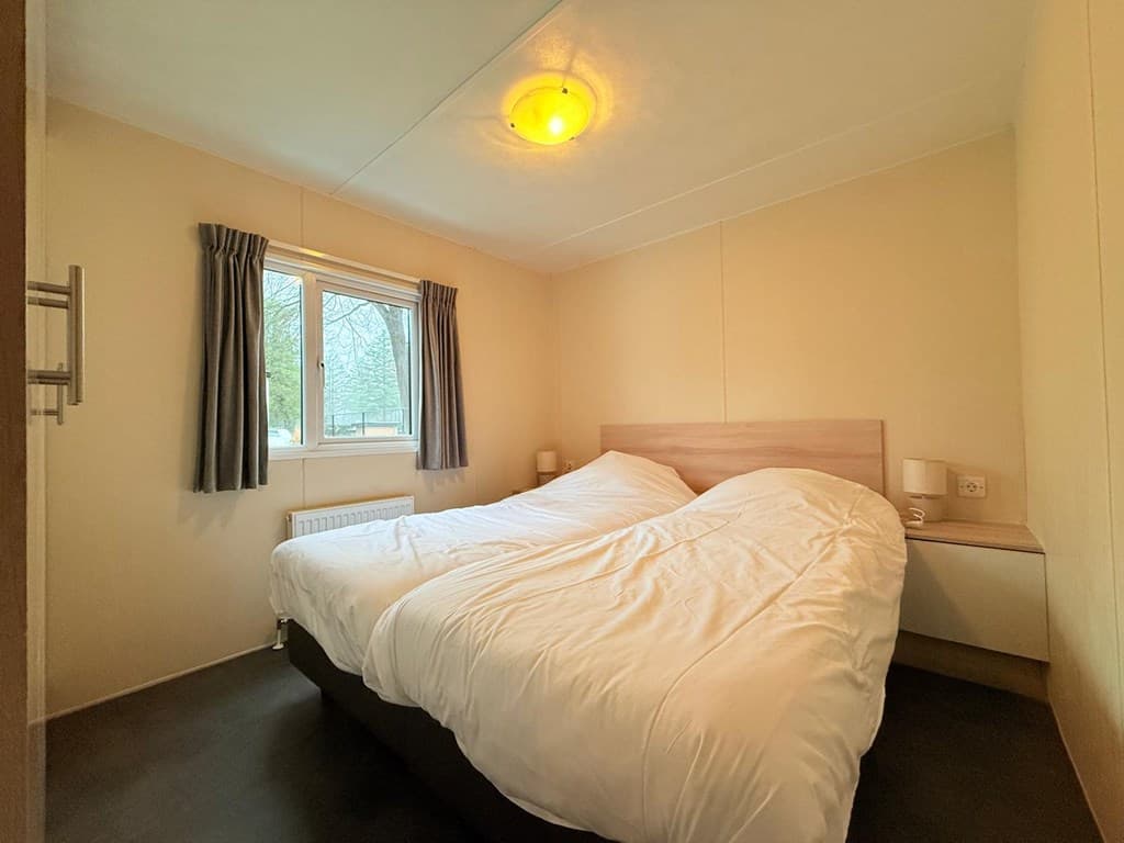 Slaapkamer met twee eenpersoonsbedden, raam, gordijnen en eenvoudige wandlampen.