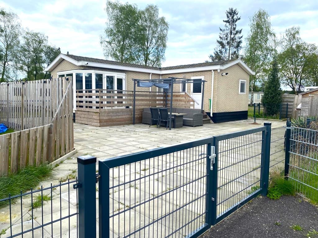 Vakantiehuis met betegeld terras, pergola en tuinmeubilair, omringd door houten schuttingen en groene bomen