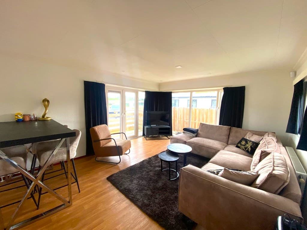 Zithoek met een bank, stoelen, tv en veel lichtinval door de grote ramen.