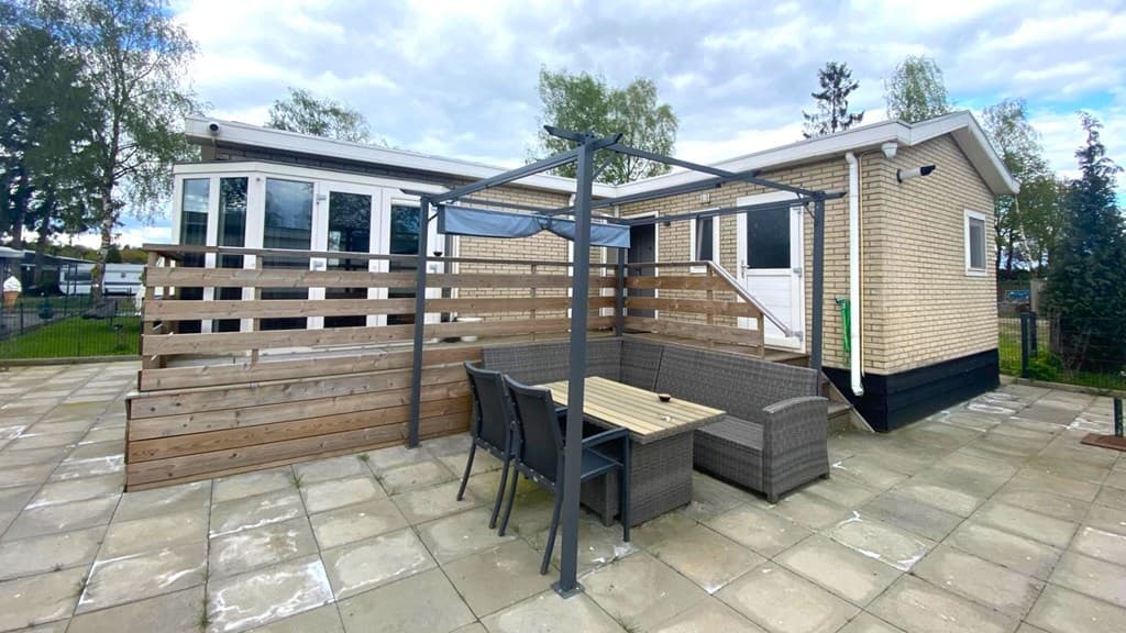 Terras met tuinmeubilair en overkapping bij een vakantiehuis in Vakantiepark De Maashorst, omgeven door begroeiing.