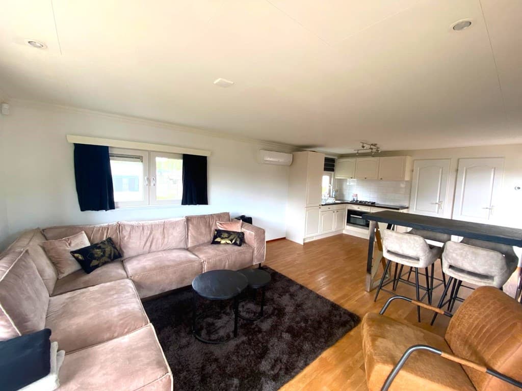 Licht interieur met een stoffen bank, eethoek en open keuken in een vakantiehuis in Vakantiepark De Maashorst.