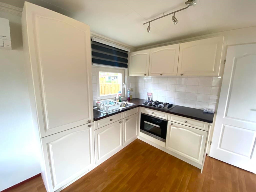 Moderne keuken met lichte kasten, gaskookplaat, oven en raam met uitzicht naar buiten.