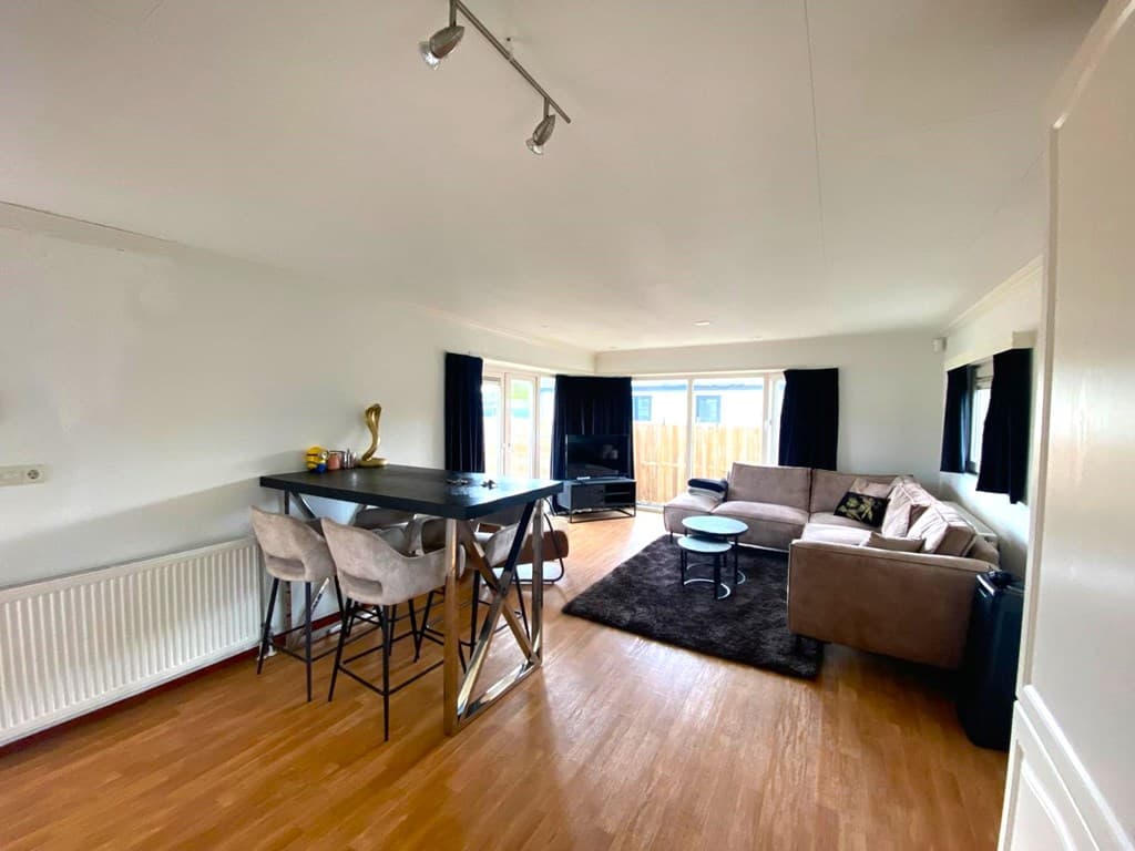 Gezellige woonkamer met eetbar, bank, tv en veel natuurlijk licht door de grote ramen.