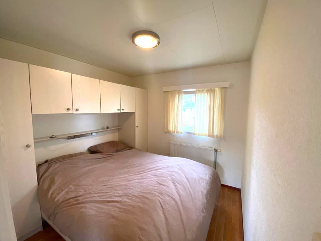 Slaapkamer met een tweepersoonsbed, kastenwand en raam met gordijnen voor natuurlijk licht.