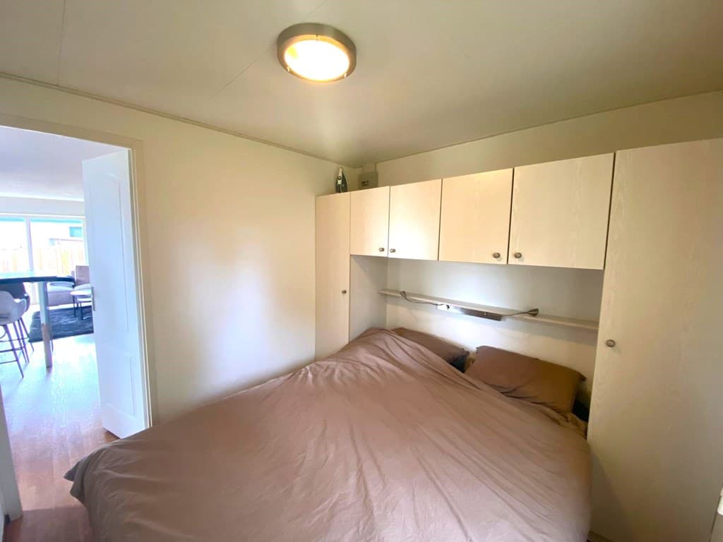 Slaapkamer met een tweepersoonsbed en kastenwand aan de muur, toegang tot een woonkamer zichtbaar via de deur
