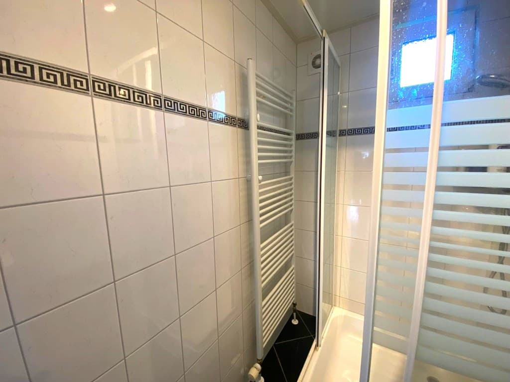 Moderne badkamer met douchecabine, handdoekradiator en witte tegels met een decoratieve rand.