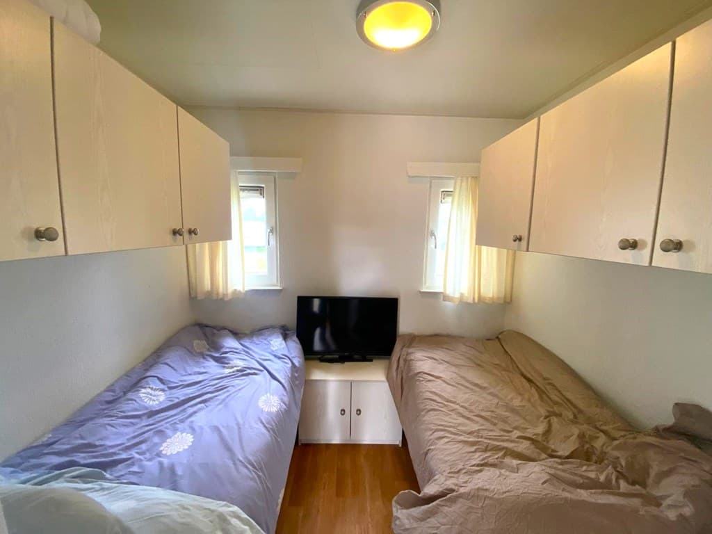 Slaapkamer met twee eenpersoonsbedden, wandkastjes, een tv en ramen met gordijnen in vakantiepark De Maashorst.