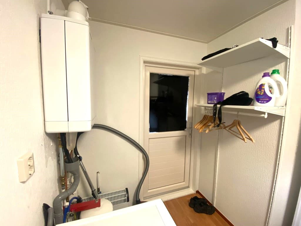 Houdruimte met een wandhangende boiler, planken en een deur naar buiten.