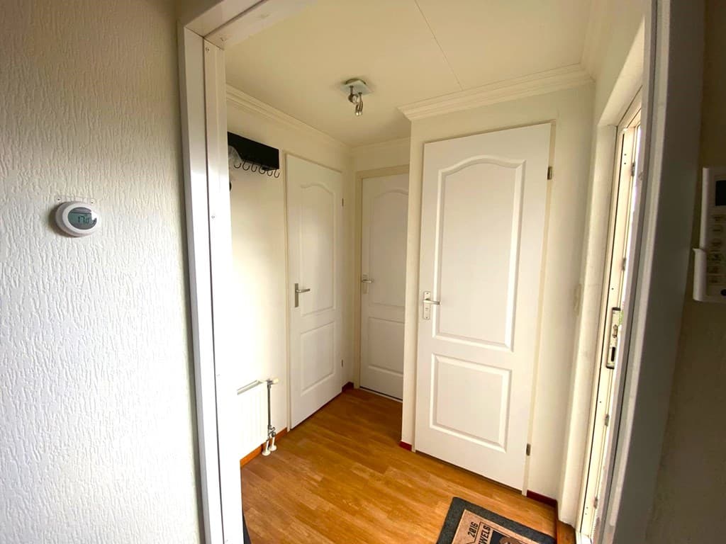 Ingang met houten vloer, witte muren en verschillende deuren naar andere ruimtes.