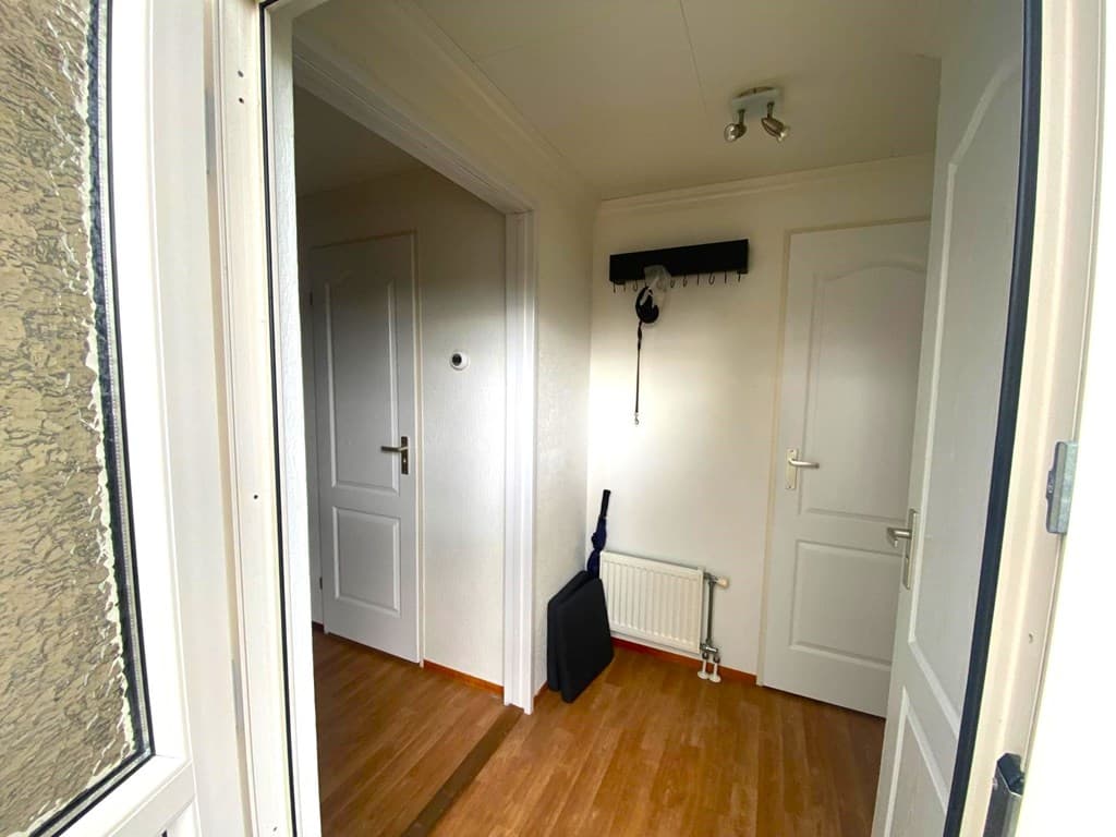 Entree van een woning met twee deuren, een verwarming en een beetje vloerbedekking in een vakantiepark.