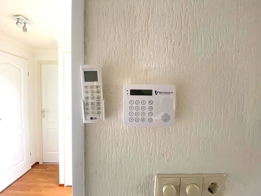 Wand met een intercom en afstandsbediening bij de ingang, lichte muren en houten vloer zichtbaar