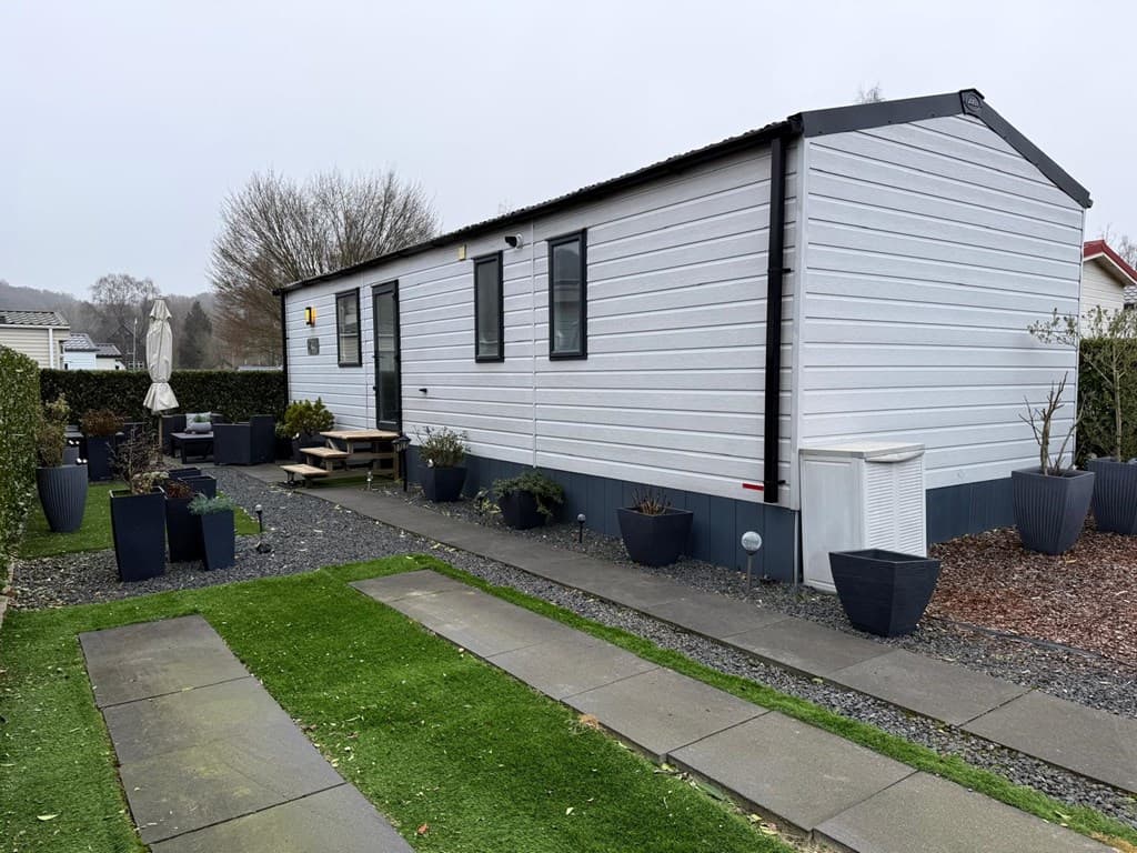 Witte vakantiewoning met een tuin en terrastegels, omgeven door plantenbakken en een grasveld