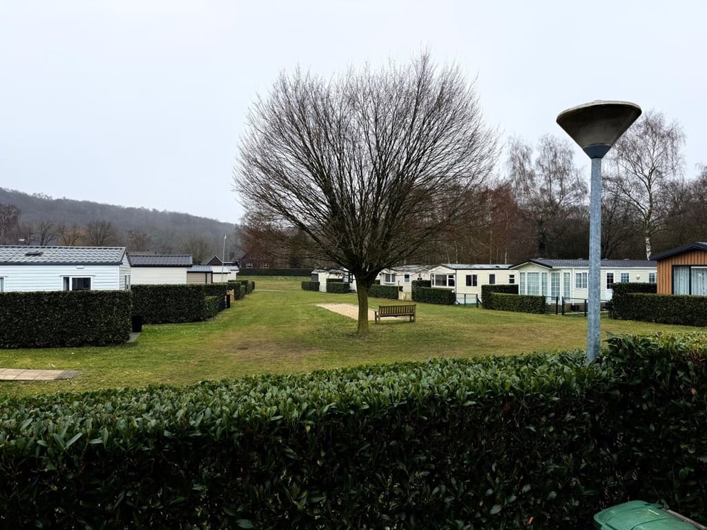 Uitzicht op een recreatiegebied met groene grasvelden, bomen, stalletjes en een bankje tussen de huisjes.