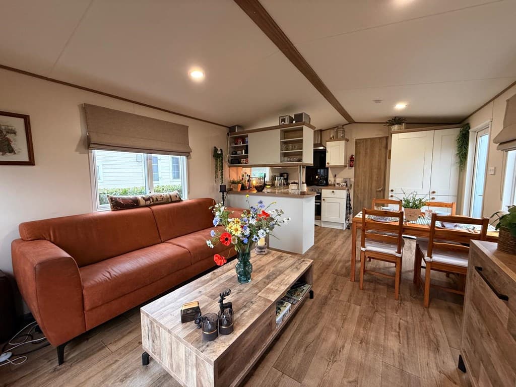 Modern ingerichte woonkamer met bank, eettafel, keuken en bloemenvaas op een houten salontafel