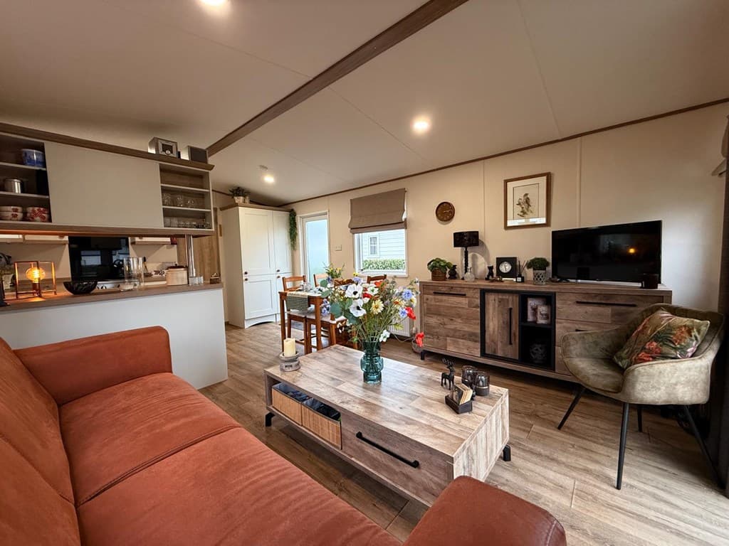 Modern interieur met een oranjetinten bank, houten meubels, een TV-meubel en een boekenkast, verlicht door natuurlijk licht.