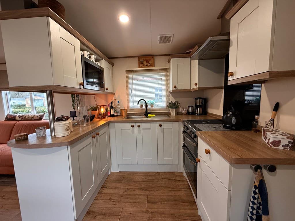 Keuken met lichte kastjes, houten aanrecht en moderne apparatuur, uitzicht op de woonkamer met een bankstel