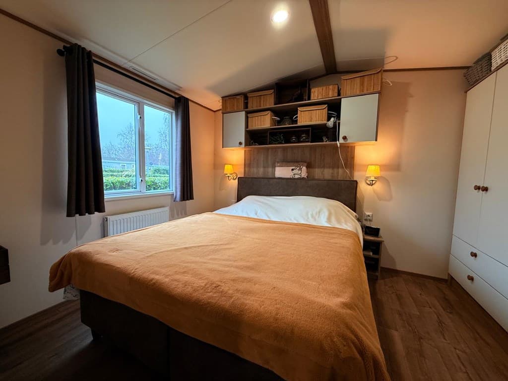 Sfeervolle slaapkamer met tweepersoonsbed, ladekast en verlichting naast het bed, raam met uitzicht naar buiten.