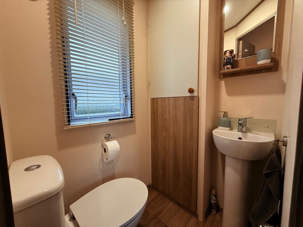 Toilet met wastafel en spiegel, gordijnen voor het raam en houten accenten aan de muur