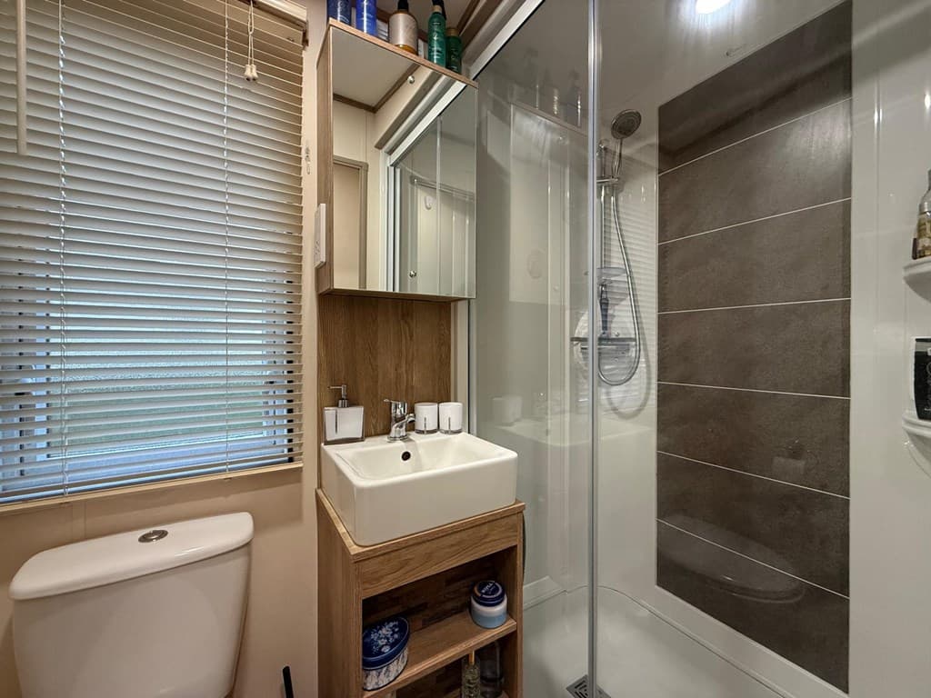 Moderne badkamer met inloopdouche, wastafel en toilet, met natuurlijke lichtinval door het raam met jaloezieën
