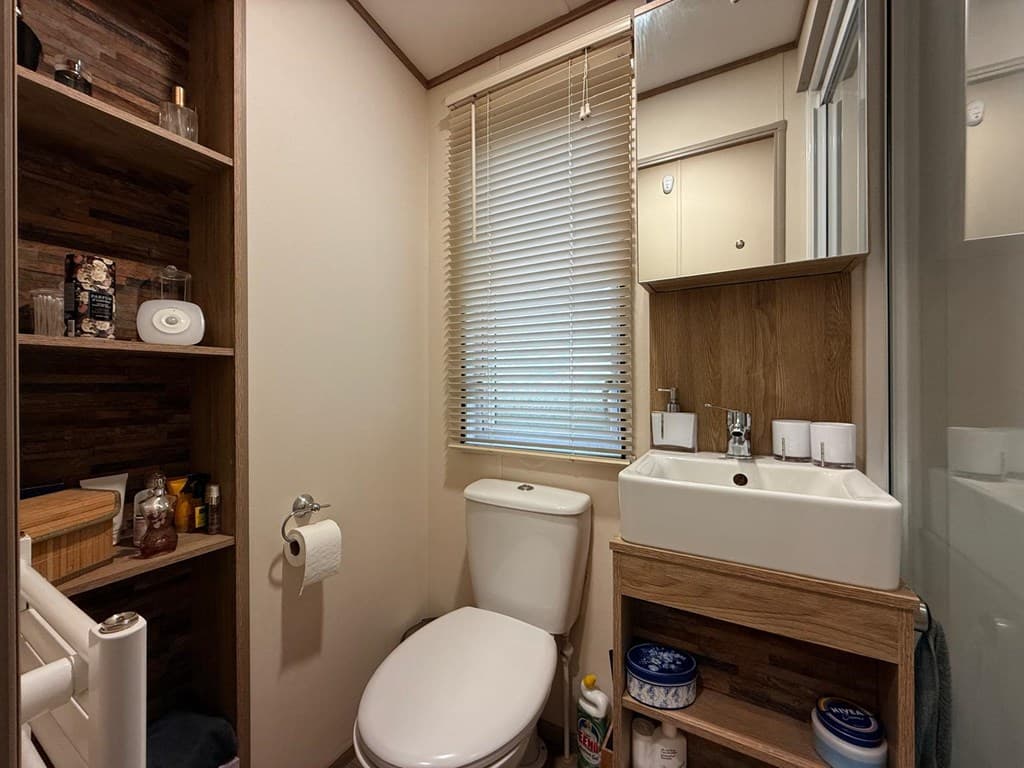 Witte wc met wastafel en kastje in een lichte badkamer met houten accenten en houten planken aan de muur