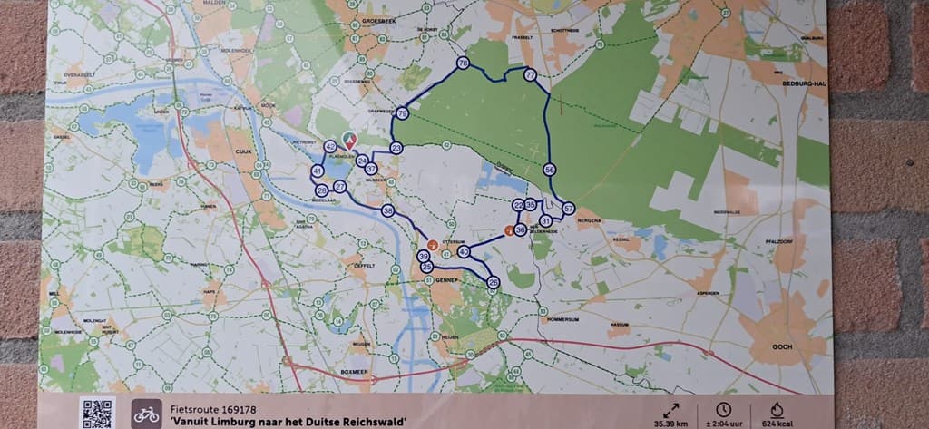 Kaart met fietsroutes van Limburg naar het Duitse Reichswald, weergegeven op een bakstenen muur met informatie over afstand e
