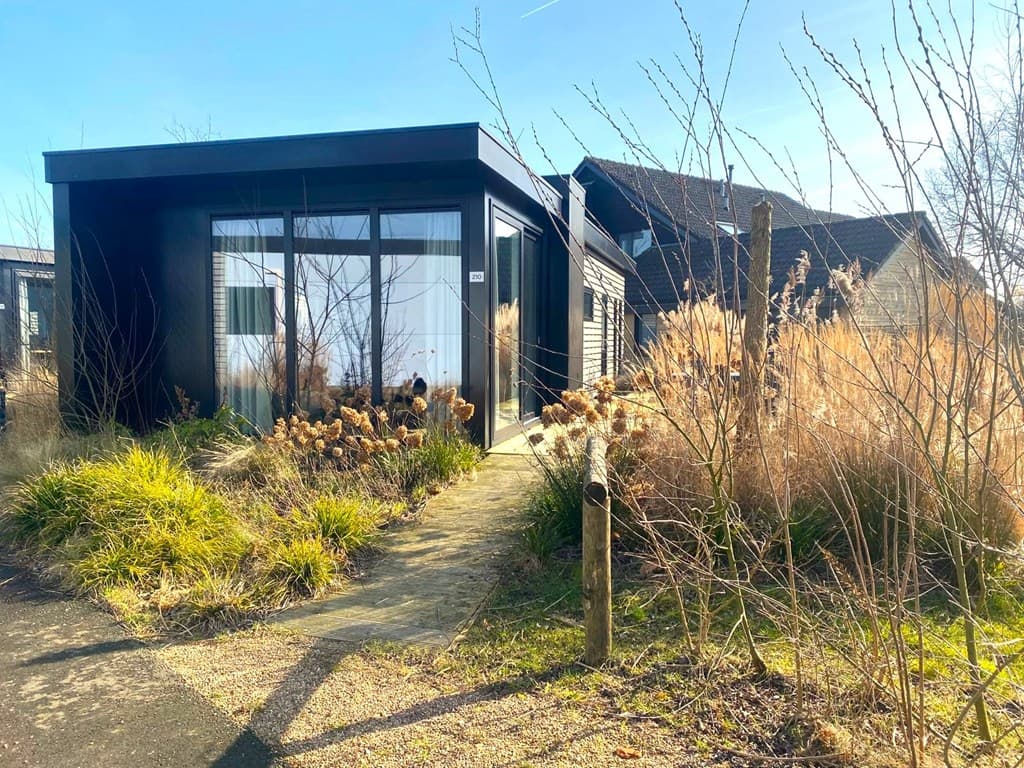Vakantiehuis in een groene omgeving met planten en een pad naar de entree, heldere lucht en een moderne uitstraling