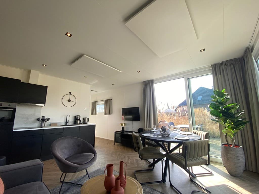Moderne woonkamer met open keuken, ronde eettafel en grote ramen met uitzicht op buitenruimte.