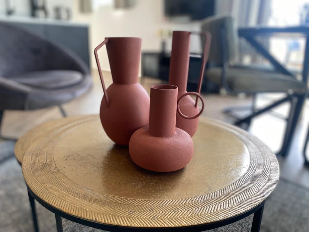 Drie decoratieve vazen in verschillende vormen en maten op een goudkleurige ronde tafel in een stijlvolle woonkamer