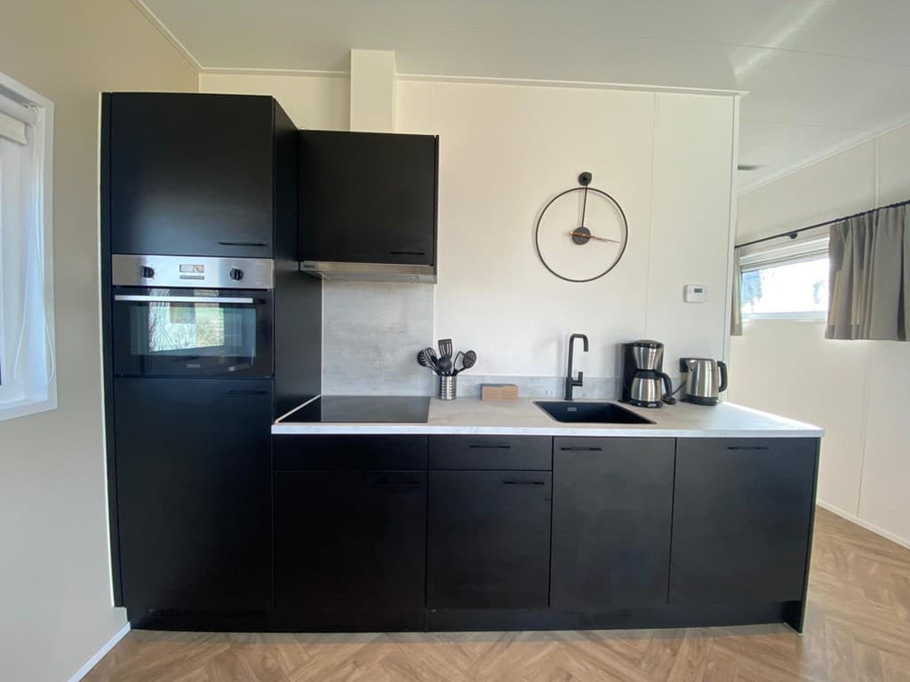 Moderne keuken in een vakantiehuis met zwarte kasten, oven, spoelbak en koffiemachine op vakantiepark De Wiedense Meren