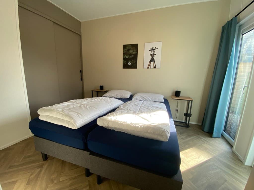 Slaapkamer met twee losse bedden, nachtkastjes en kunst aan de muur, grote ramen met uitzicht naar buiten.