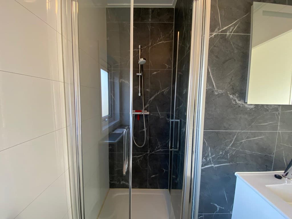 Moderne inloopdouche met glazen wand en marmerachtige tegels in een lichte badkamer