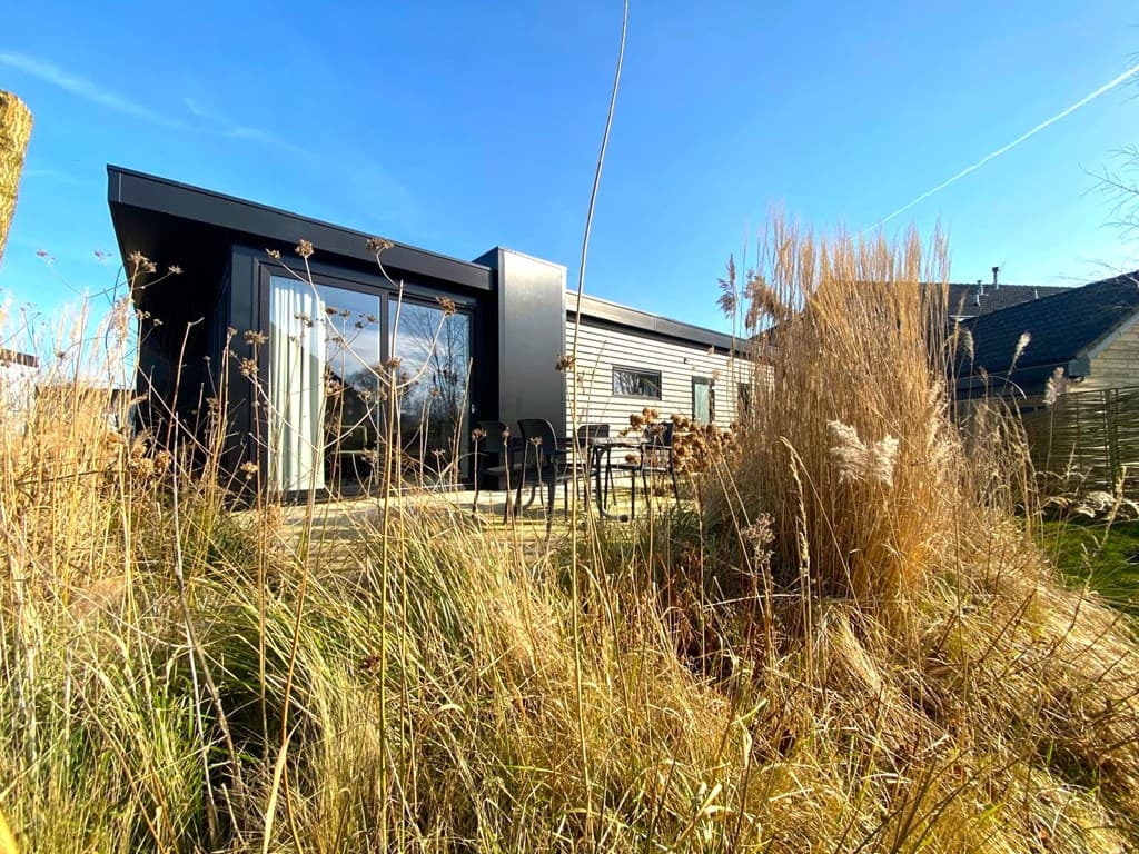 Moderne vakantiewoning met grote ramen, uitzicht op gras en riet, terras met tuinmeubelen in De Wiedense Meren