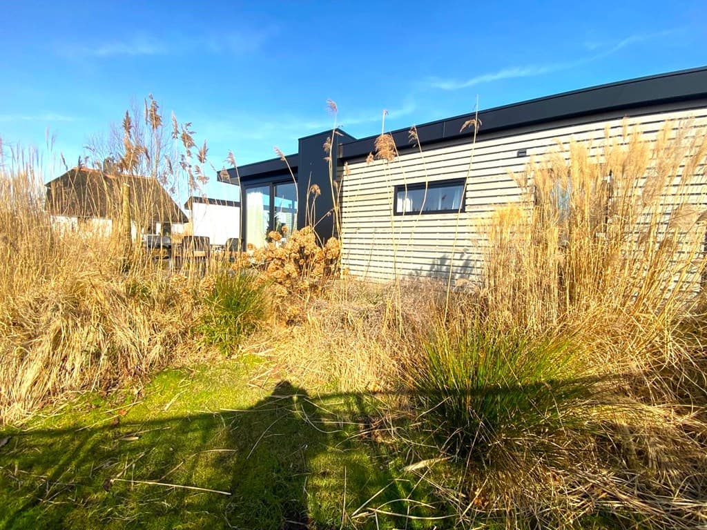 Moderne vakantiewoning omgeven door hoge grasplanten en een helder blauwe lucht in Wanneperveen