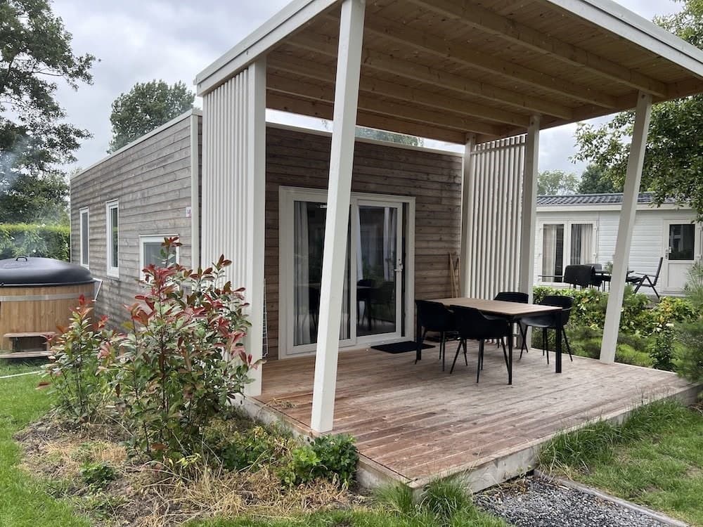 Houten vakantiewoning met overdekt terras en eettafel, omgeven door groen en een tuin.