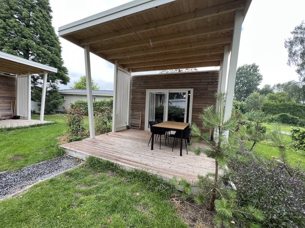 Terras met houten vloer en tafel met stoelen, omringd door groen en bomen bij een woning in EuroParcs De Biesbosch.