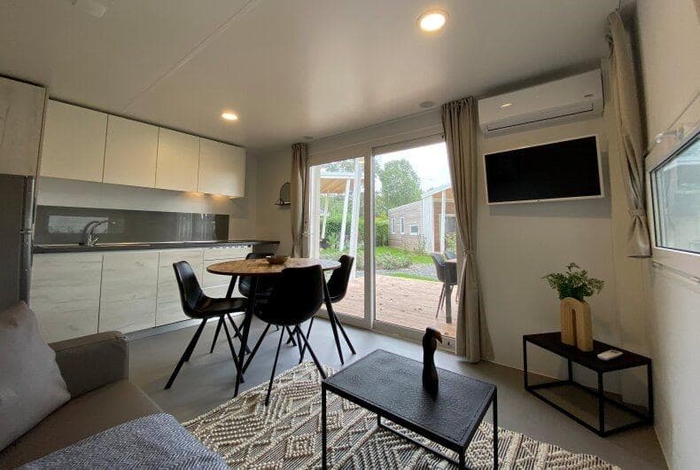 Moderne woonkamer met open keuken, eetgedeelte en schuifdeur naar het terras met tuinzicht.