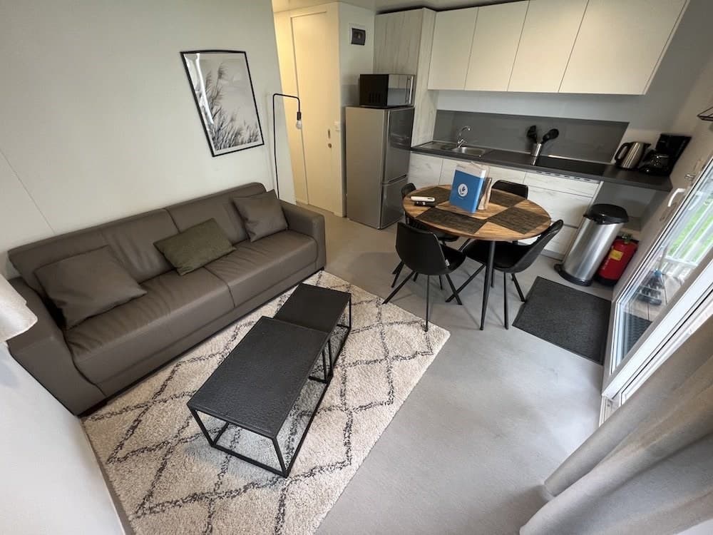 woonkamer met bank, tafel en stoelen, open keuken met koelkast en aanrecht, lichte en moderne inrichting