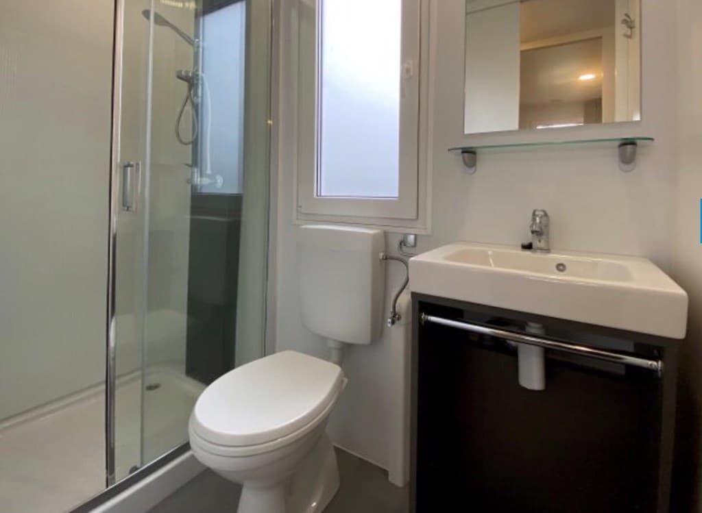 Moderne badkamer met douche, wastafel en toilet, grote spiegel en raam voor natuurlijke lichtinval