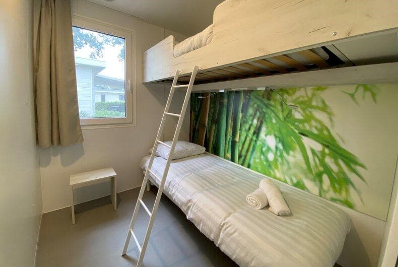 Kamer met stapelbed, een eenpersoons bed, een klein bureau en een raam met uitzicht op de buitenlucht.