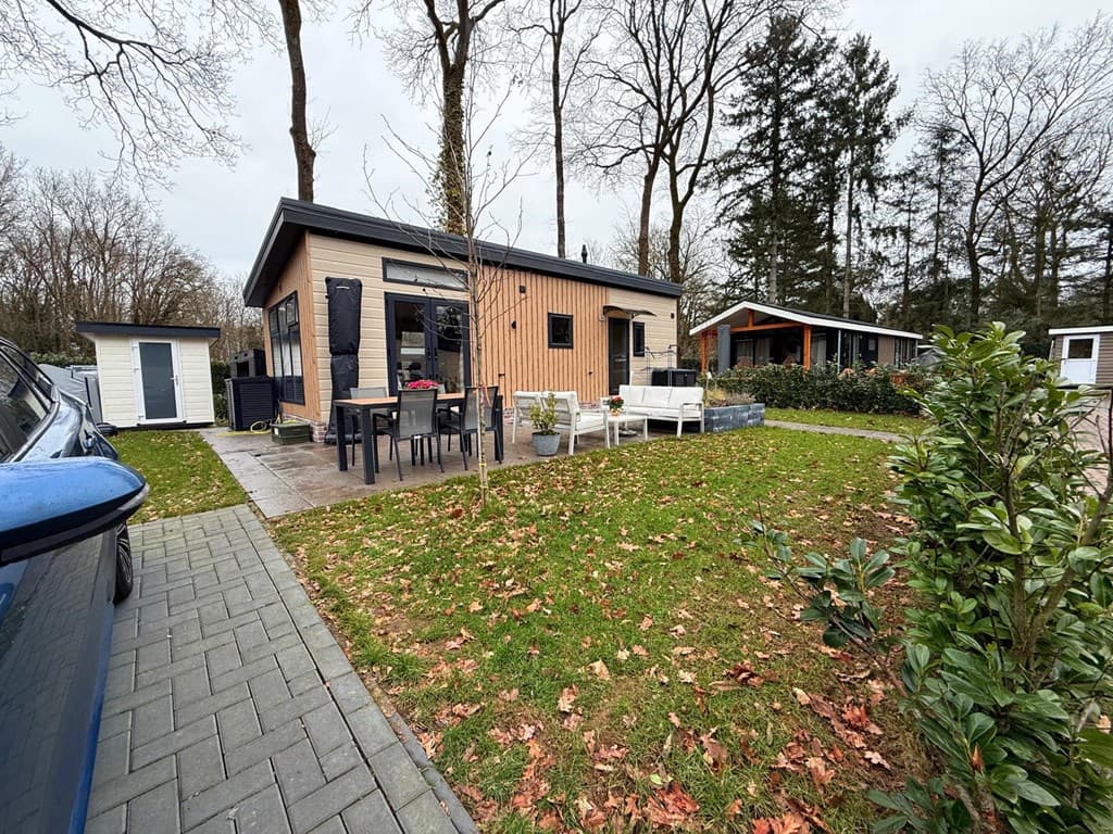 Houten vakantiehuisje met terras en tuinmeubilair, omringd door bomen en gras, gelegen op camping De Konijnenberg.