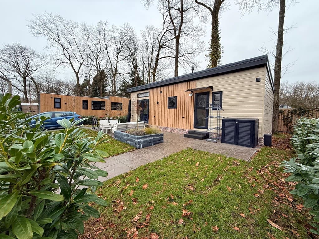 Buitenzicht op een vakantiewoning met een groene tuin, naast een andere accommodatie en omgeven door bomen.