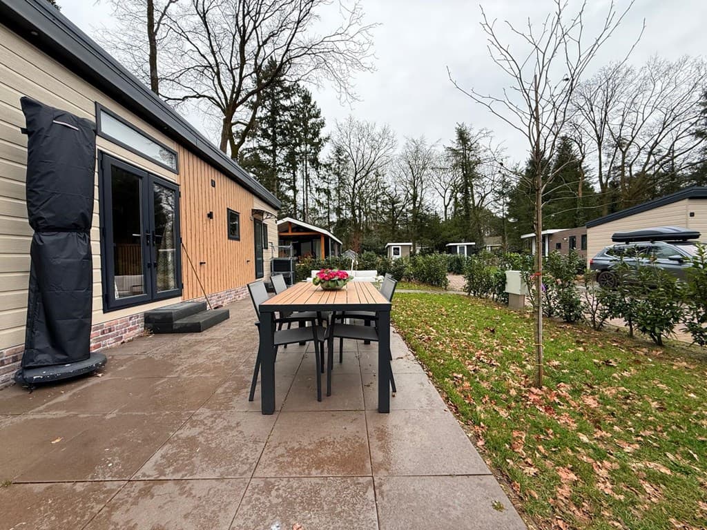 Terras met een tafel en stoelen, omringd door groen met uitzicht op andere vakantiehuisjes en bomen