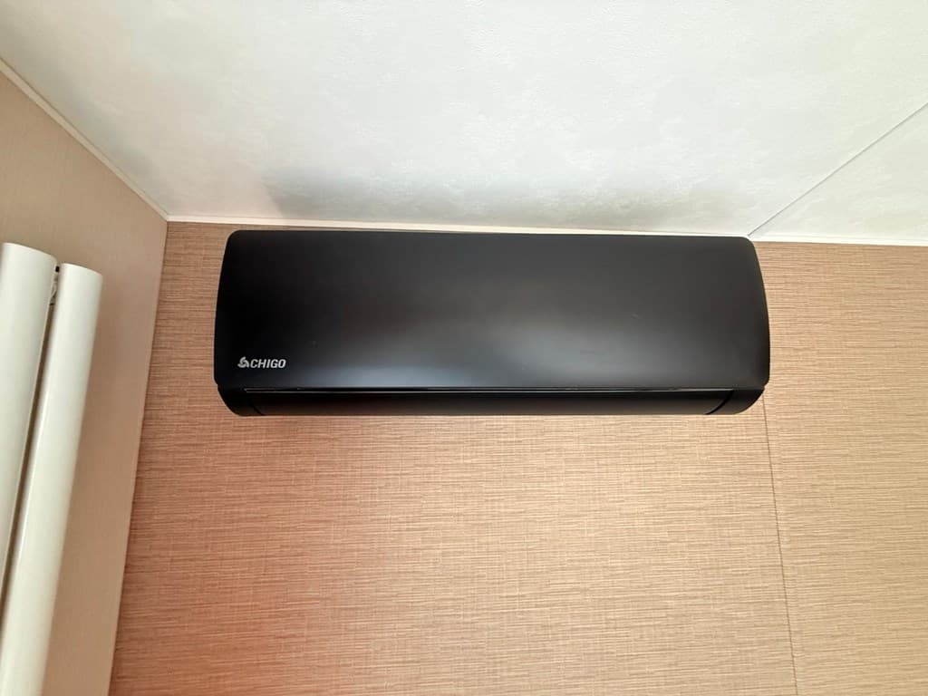 Zwarte luchtverwarmer aan de wand in een ruimte met beige wandafwerking.