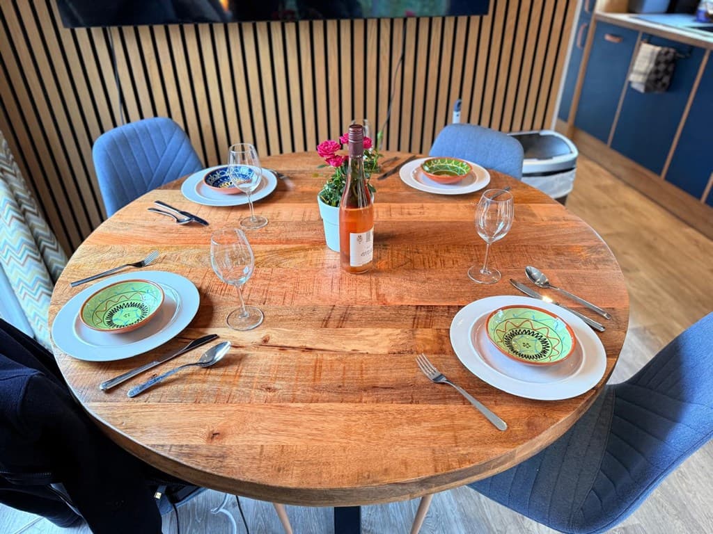 Eettafel met vier borden, glazen en een fles wijn, omringd door twee stoffen stoelen met een houten vloer.