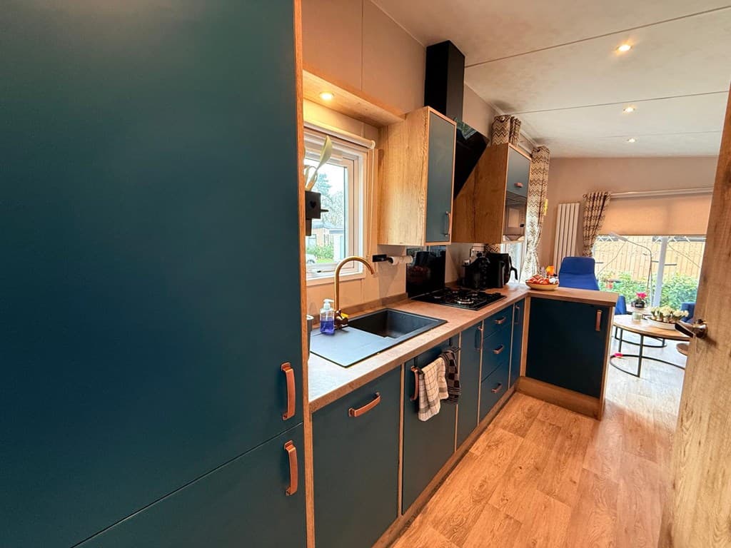 Keuken met blauwe kasten, aanrecht en ramen met uitzicht op de tuin, voorzien van kookplaat en afzuigkap.
