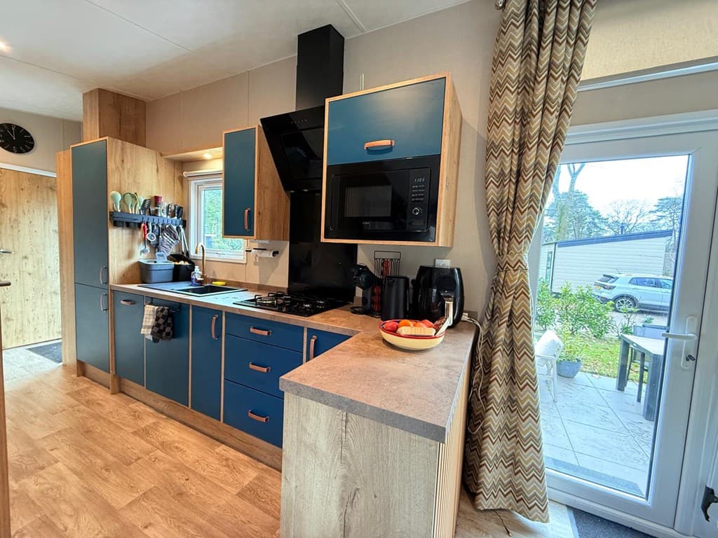 Moderne keuken met blauwe kasten, gasfornuis, oven en natuurstenen aanrecht, met uitzicht op de tuin via een glazen deur