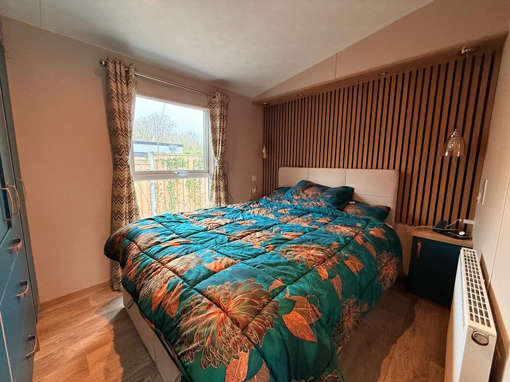 Slaapkamer met een tweepersoonsbed en een raam met uitzicht naar buiten, afgewerkt met houten accenten en kleurrijke bedding