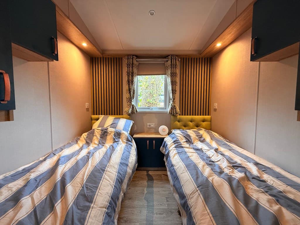 Slaapkamer met twee eenpersoonsbedden, een nachtkastje en gordijnen tegen een achtergrond van houten elementen.