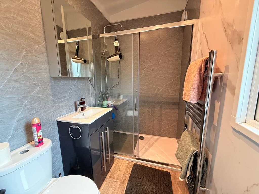 Moderne badkamer met inloopdouche, wastafel en handdoekradiator, betegelde wanden en houten vloer.